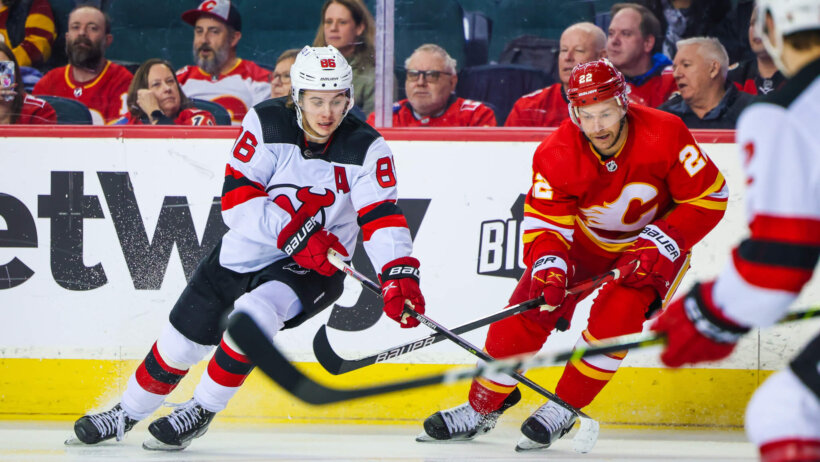 New Jersey Devils center Jack Hughes and Calgary Flames center Trevor Lewis battle for the puck