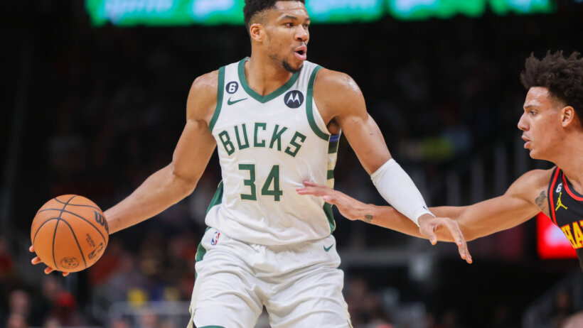 Giannis Antetokounmpo holds a defender at arm's length