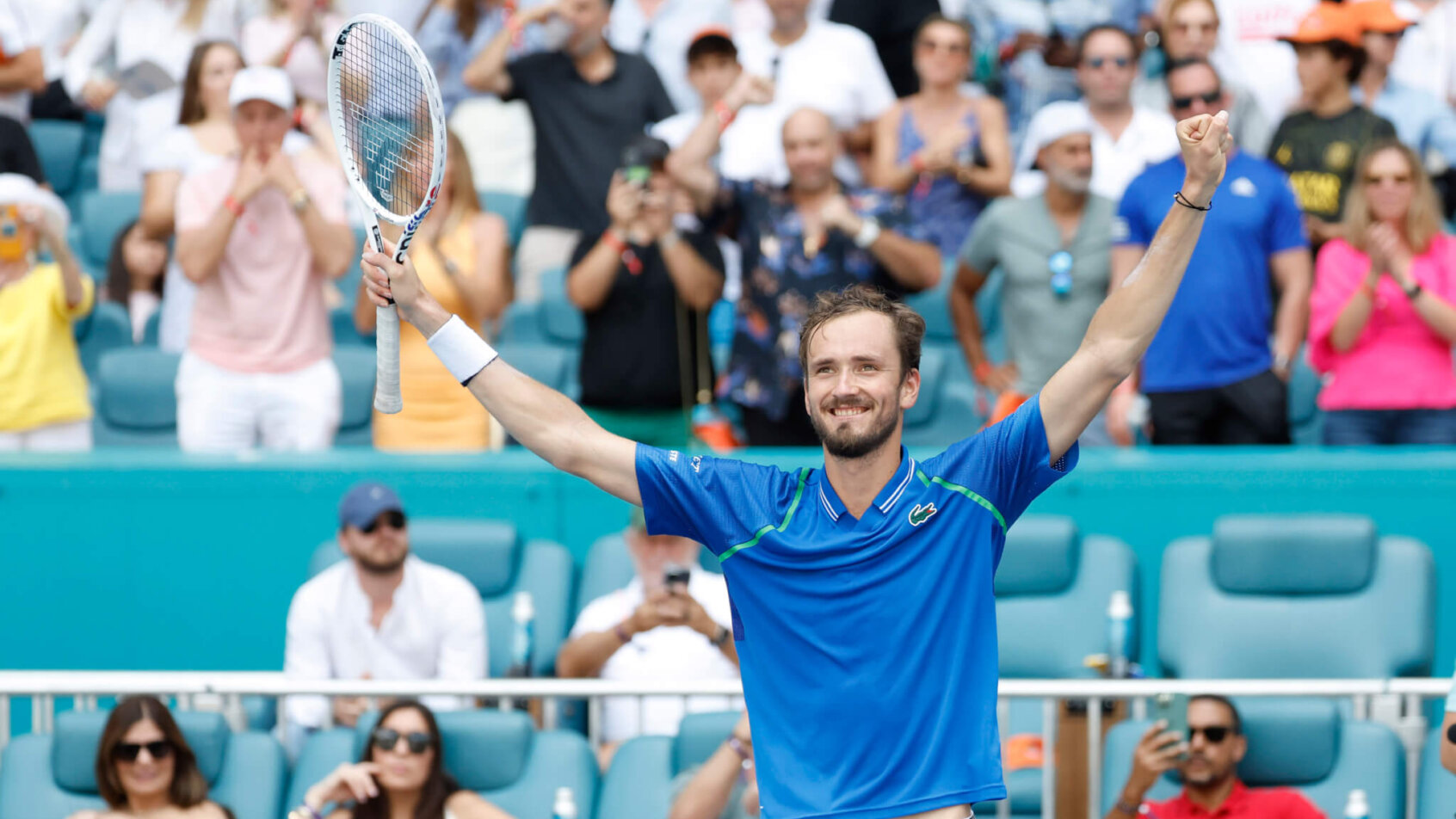 Daniil Medvedev celebrating with his hands in the air after winning a tennis match.