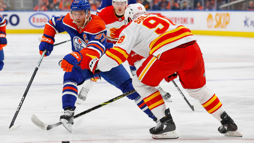 Edmonton Oilers forward Connor McDavid tries to carry the puck around Calgary Flames defensemen Ilya Solovyov