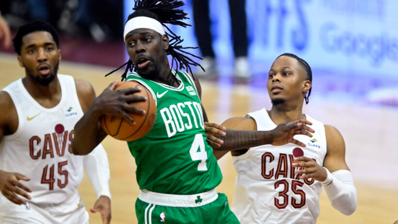 Boston Celtics guard Jrue Holiday controls a rebound as a pair of Cleveland Cavaliers look on